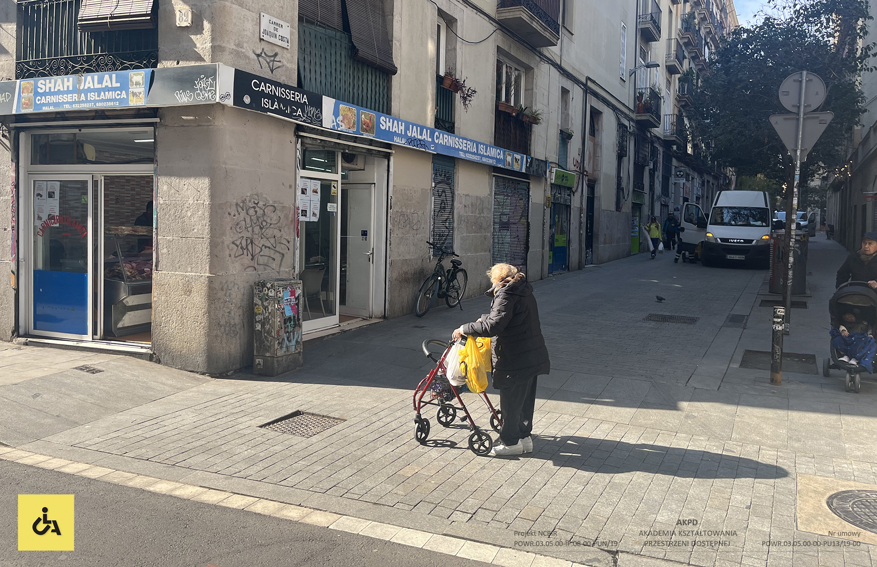 Osoba niepełnosprawna z chodzikiem na chodniku, w tle budynek, centrum miasta